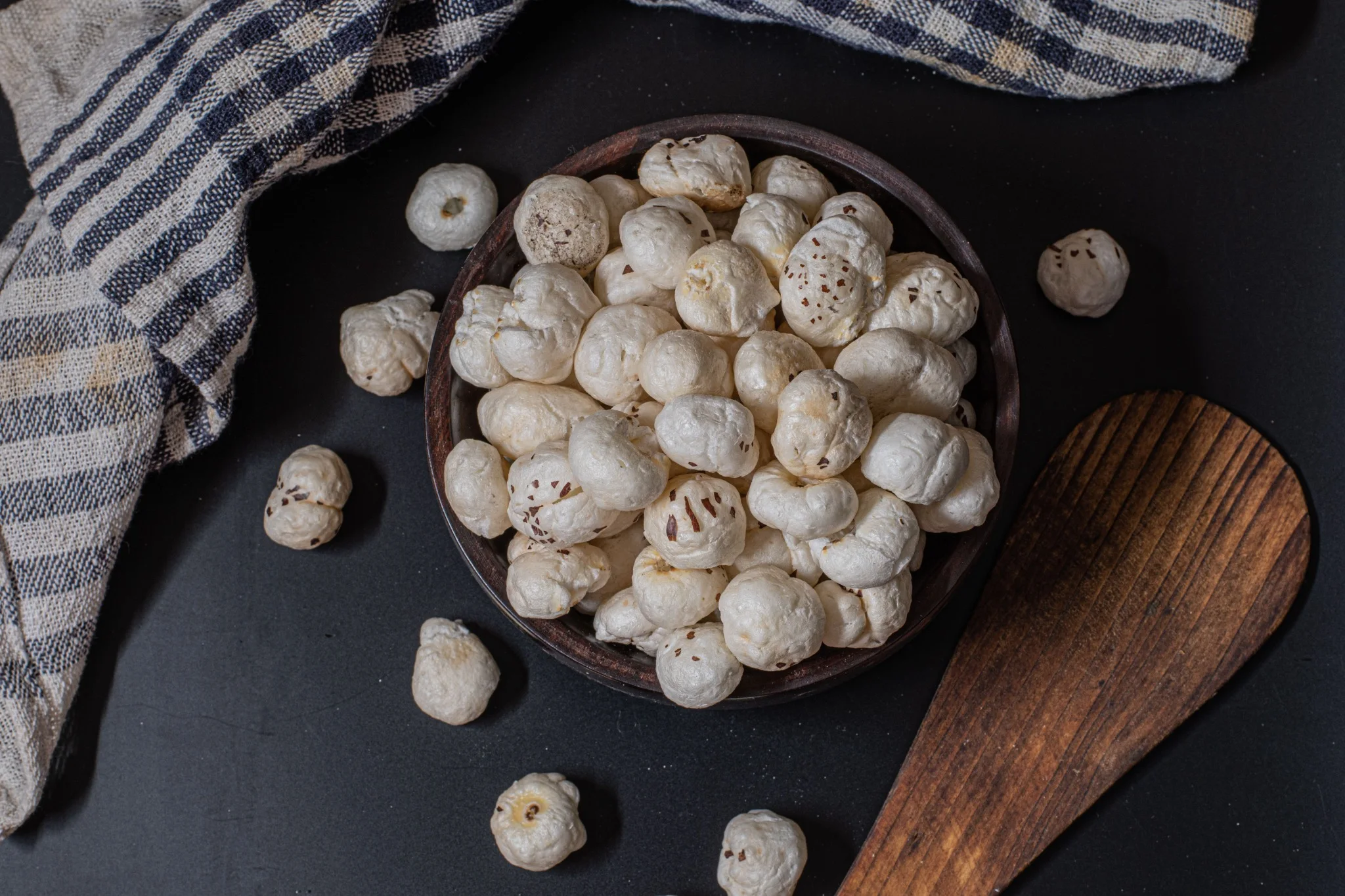 Real popped makhana in a wooden bowl, with a wooden spoon and linen cloth